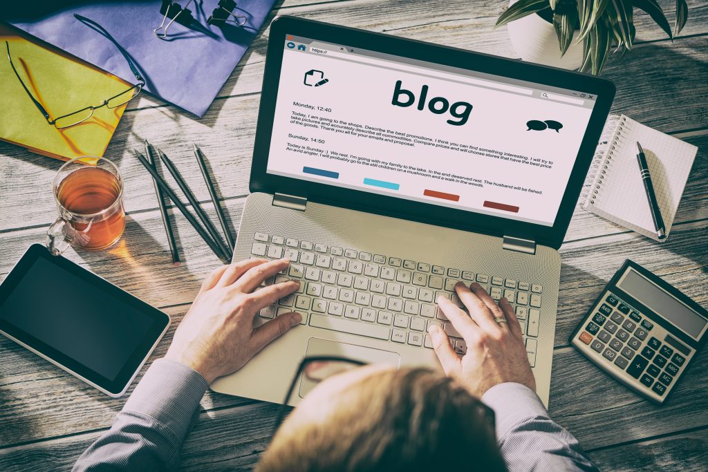 Overhead photo of man writing on laptop with blog written on screen